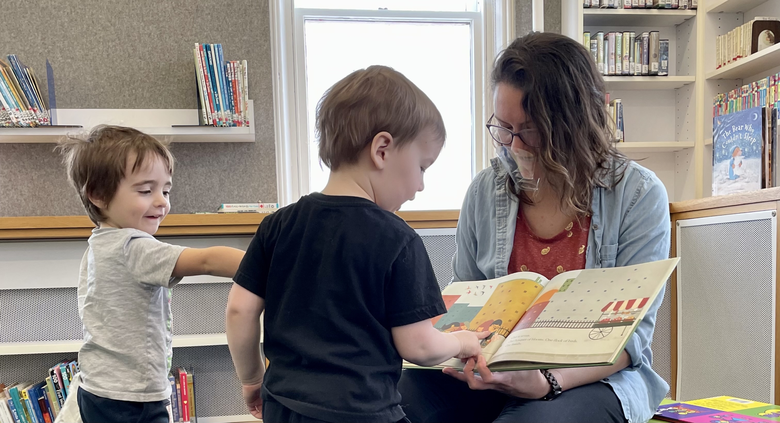 A library staff member reads a picture book to two young children at story time.